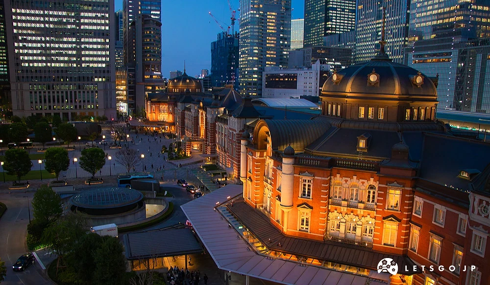 東京車站紅磚建築夜景,建築與後方現代高樓群皆亮起暖黃燈光。